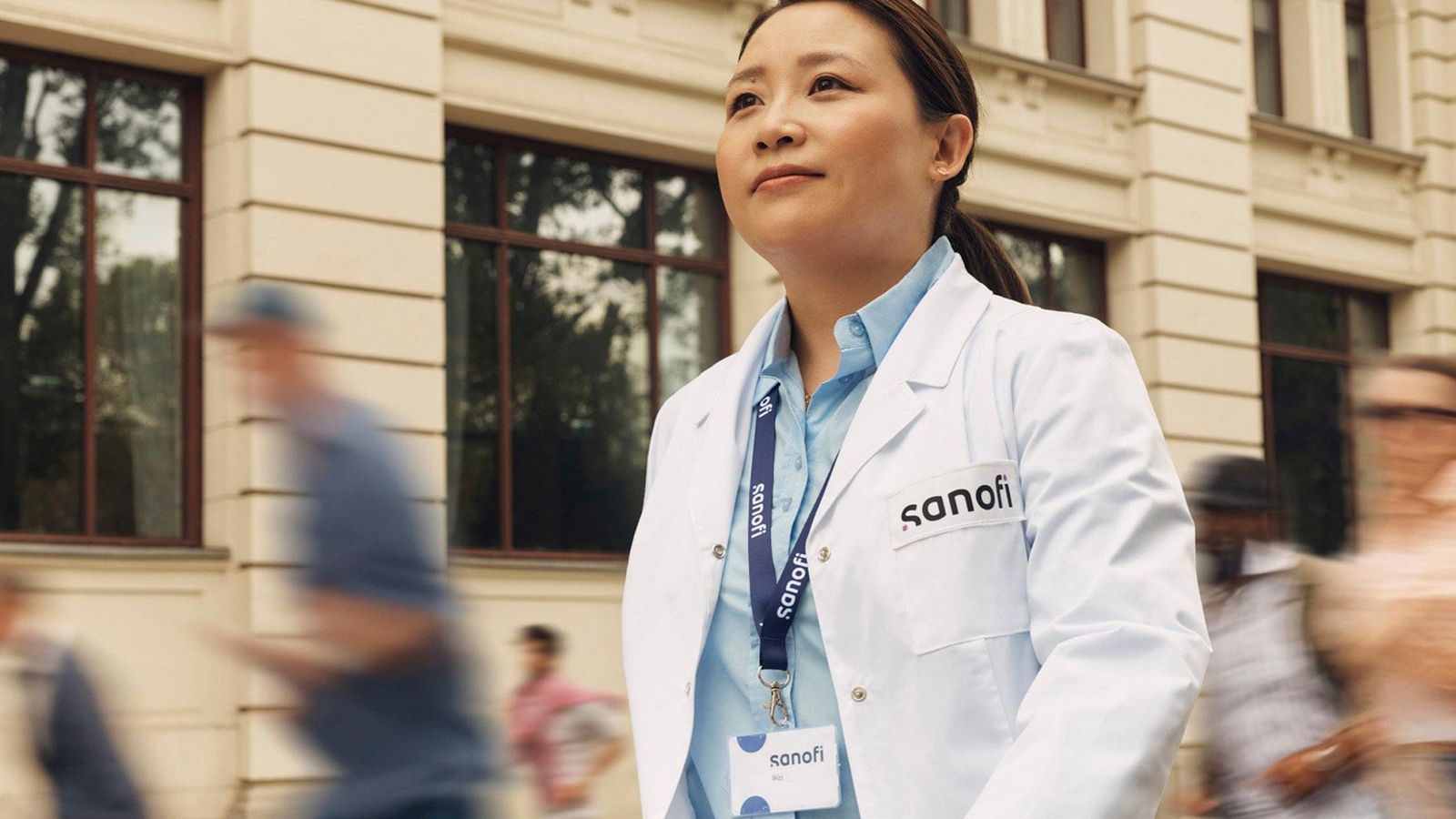 a Sanofi employee walking on the street, wearing her Sanofi badge and a scientist's white coat