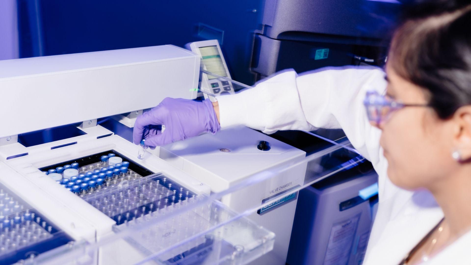 Un technicien, portant des gants violets et des lunettes de sécurité, effectuant une analyse structurale par HDX-MS, manipulant des échantillons avec précision.