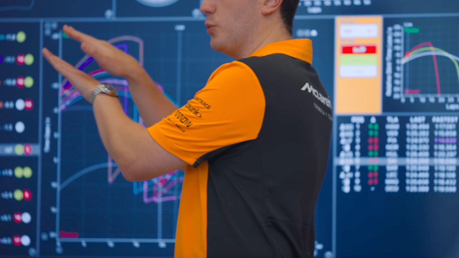 McLaren Racing engineer analyzing Formula 1 performance data on a multi-screen dashboard, illustrating the precision analytics and AI-powered systems Sanofi applies to pharmaceutical manufacturing and supply chain optimization for medicines and vaccines production across its global network.