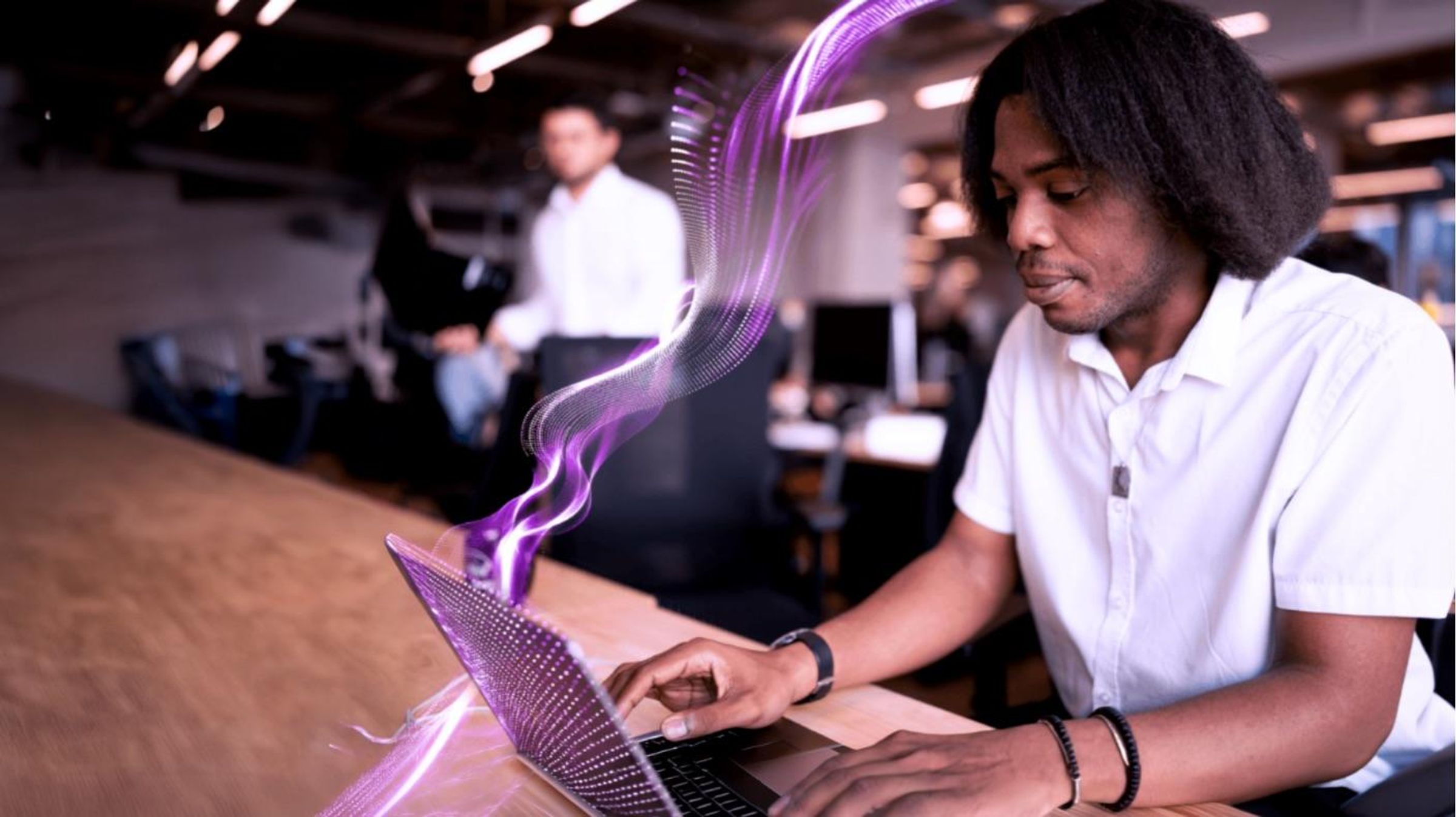 Man working on laptop in modern office with colleague in background
