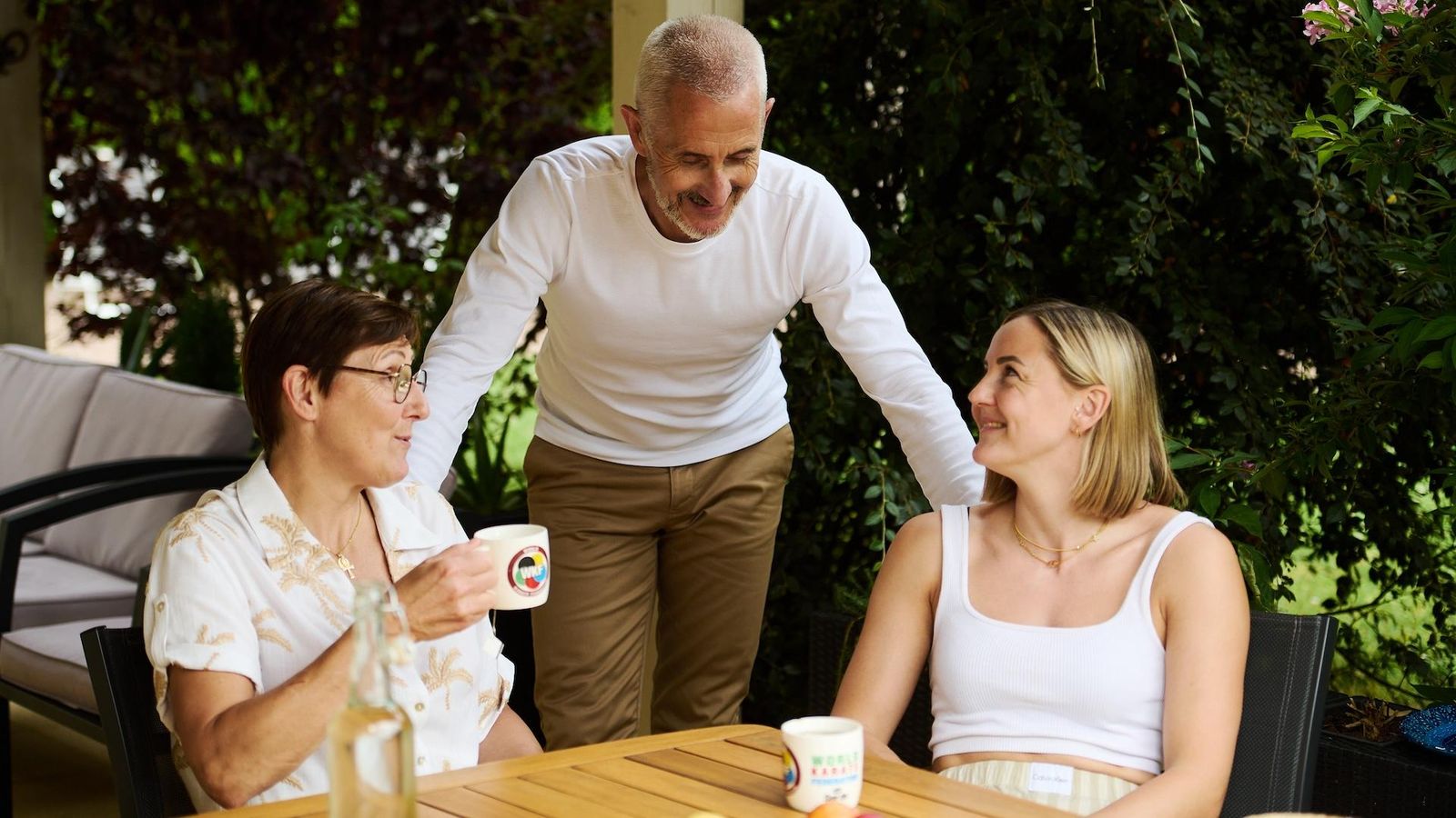 Alizée’s father standing behind his wife and Alizee Agier, a women with Type 1 Diabetes who are seated at a table in a home setting.