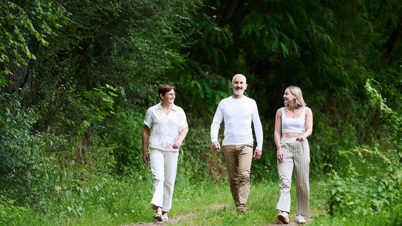 A family of three – Alizée a woman living with type 1 diabetes  and both parents - walking along a forest path surrounded by tall trees. They appear to be enjoying a nature walk together