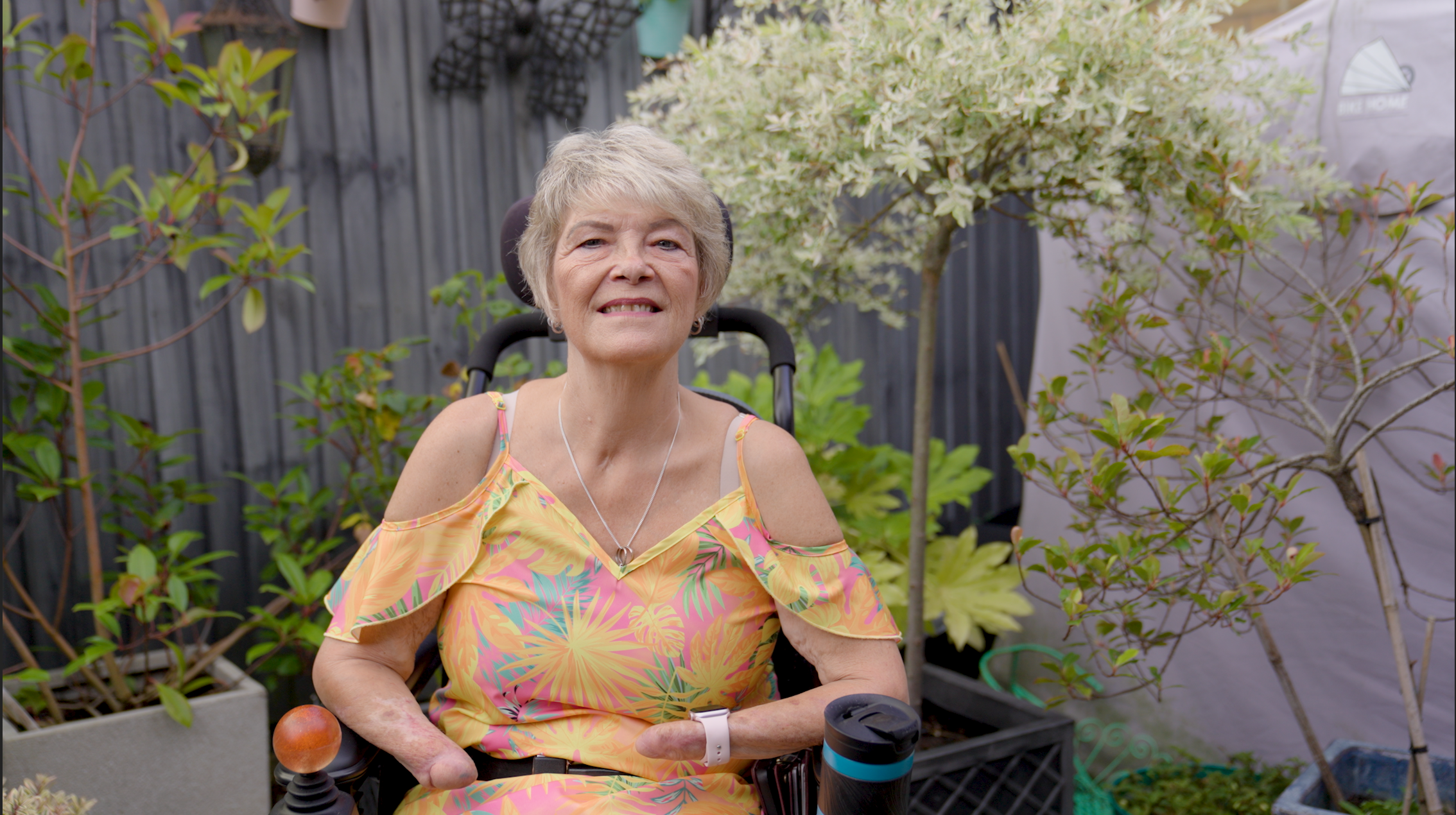 An older woman sitting in a wheelchair in a vibrant garden filled with blooming flowers.