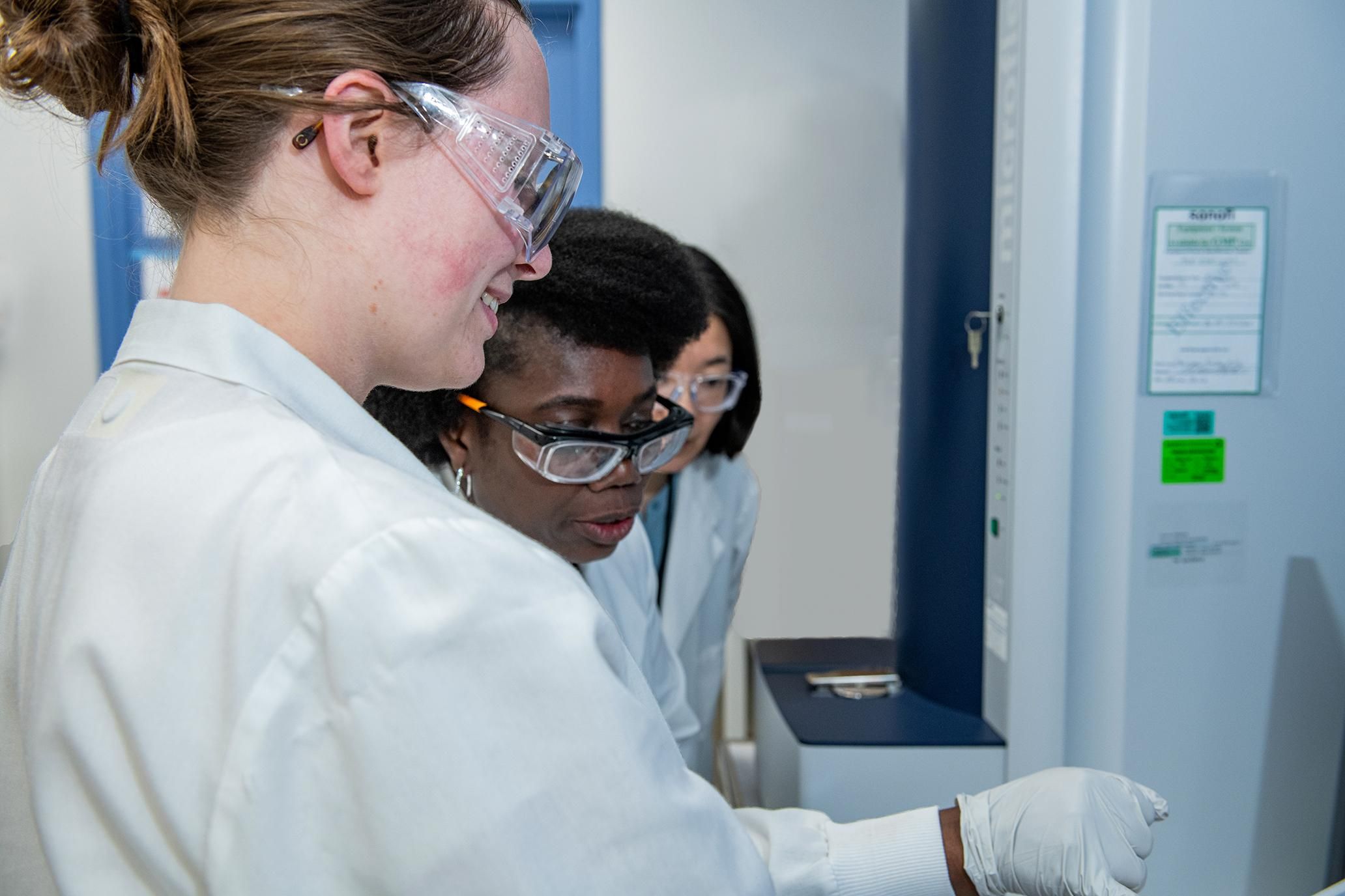 Mathilde Scheuber smiles as she shows something on a screen to two female colleagues, all wearing white lab coats