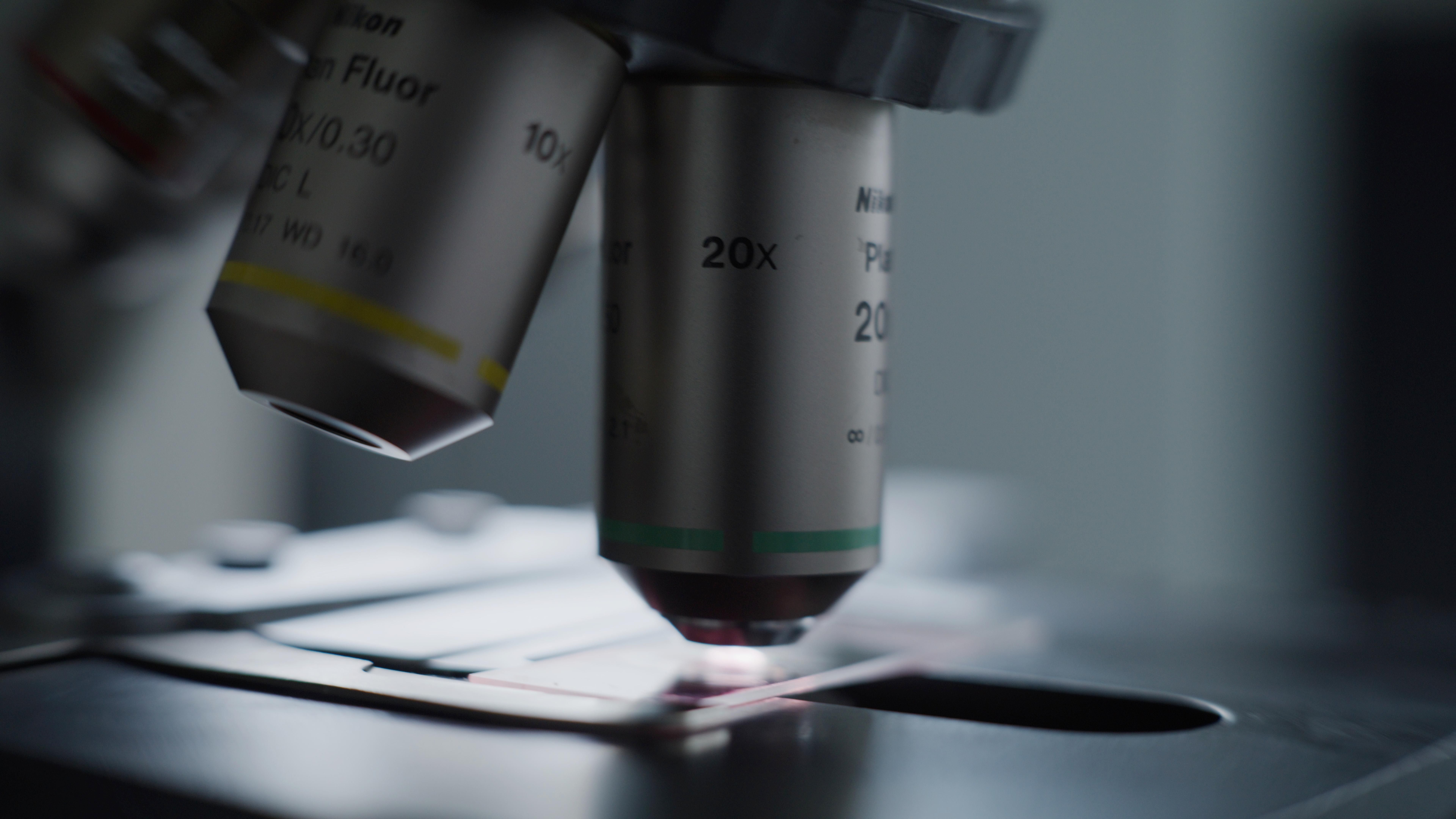 Close-up of a microscope lens, showing 20x magnification. The lens focuses on a glass slide under the microscope.