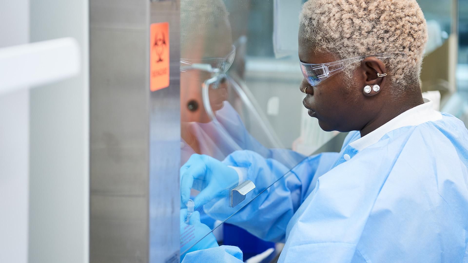 Elsa Diffo Tiayo, is wearing safety glasses and a blue lab outfit and gloves, and is working under a fume hood