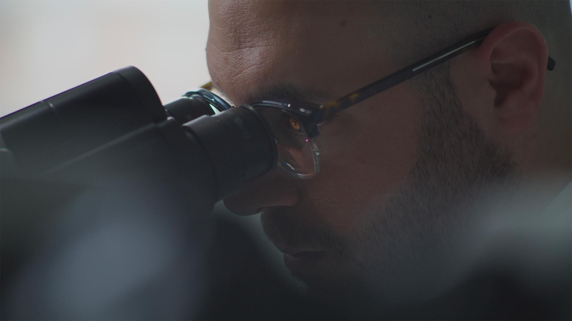 Nizar El Murr, with glasses and a short black beard, looking in a microscope