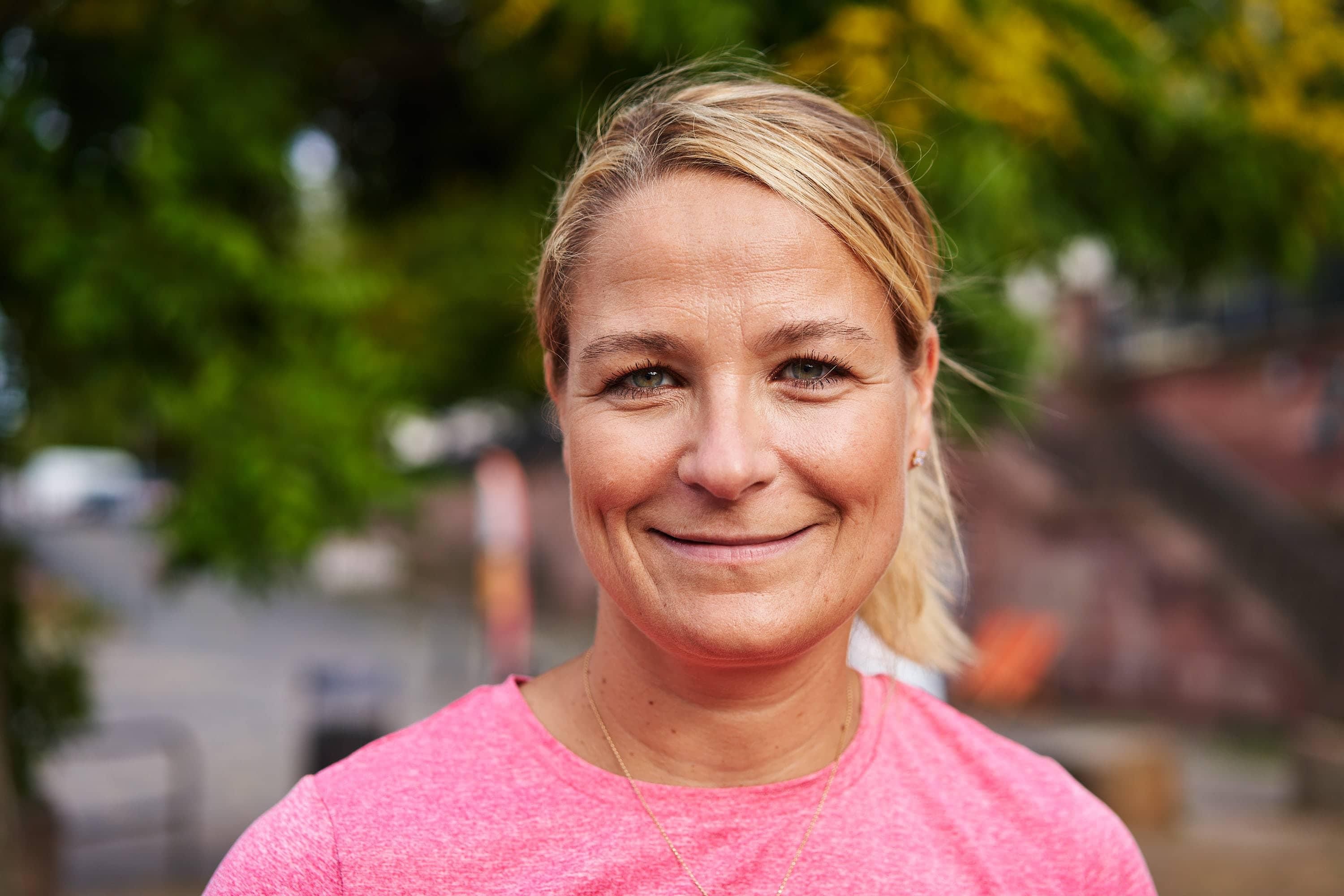 Un primer plano de Caroline Blechschmidt. Lleva el pelo rubio recogido, una amplia sonrisa, una camiseta rosa y un collar.