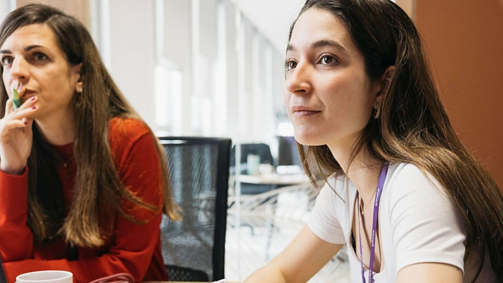 Woman with long hair sitting with colleagues, pen in hand, listening to her interlocutors.