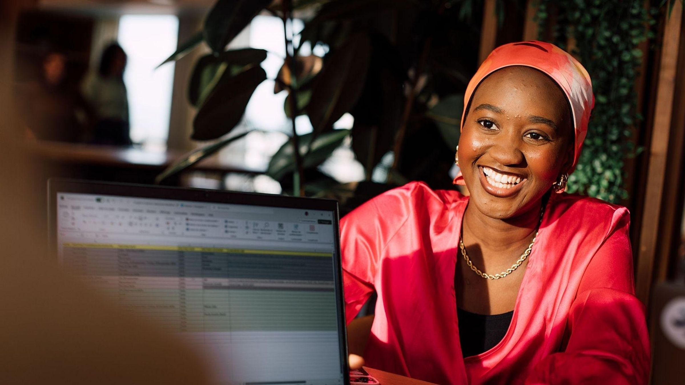 Woman wearing a turban and a red blouse, smiling, looking at the person in front of her.