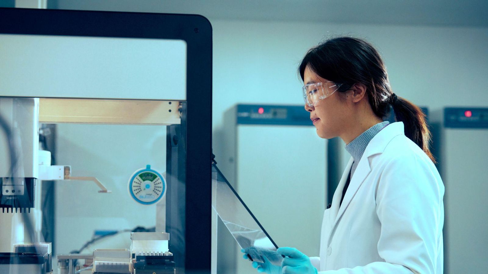 Shuang Yang, a Scientist at Sanofi China, conducting research in a professional laboratory setting. She is wearing a white lab coat and protective gloves while working with scientific equipment, surrounded by lab apparatus.