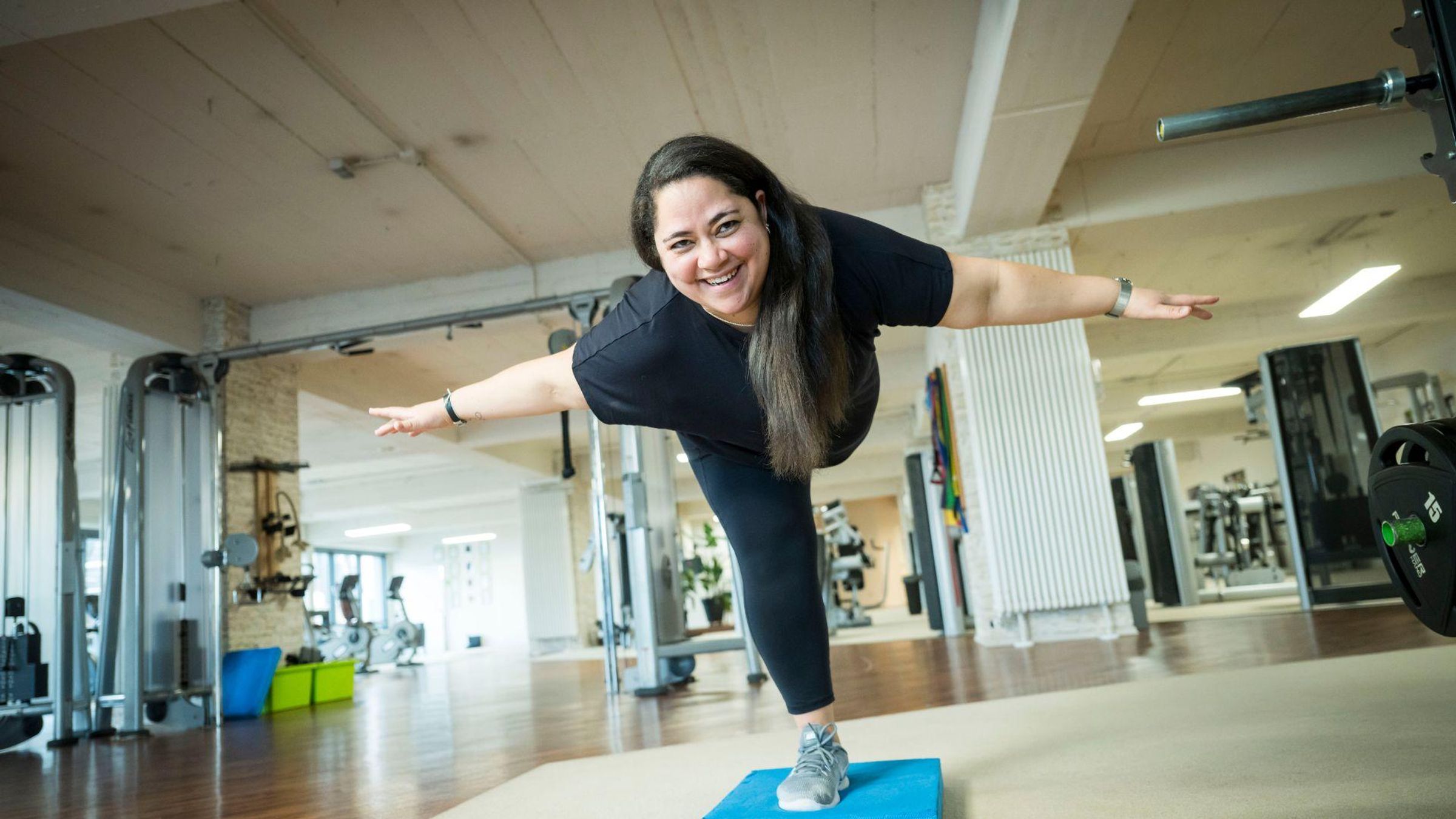 Woman balancing on one leg during exercise in a gym.