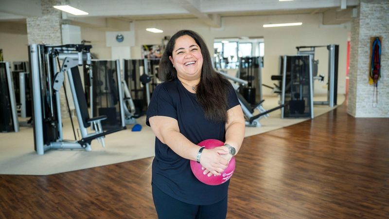 Woman smiling while holding a pink exercise ball in a gym.
