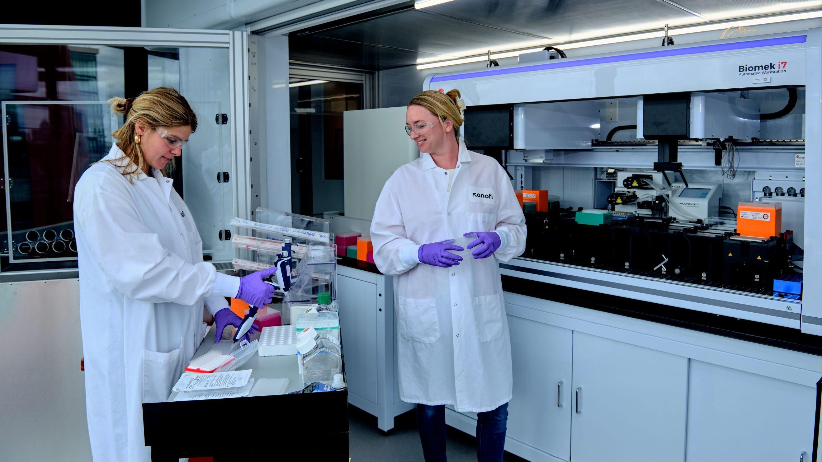 Laura Powers and Kelly Balko wearing lab gear and testing samples in their lab.