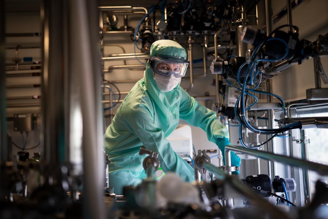 Karine Roblot, wearing a light green protective suit, operating steel equipment with lots of valves, gauges and tubing