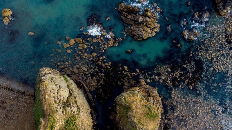 An straight down drone view of Garrarus beach, Waterford Ireland, with sea green waters, coarse sandy beach, and a rocky coast