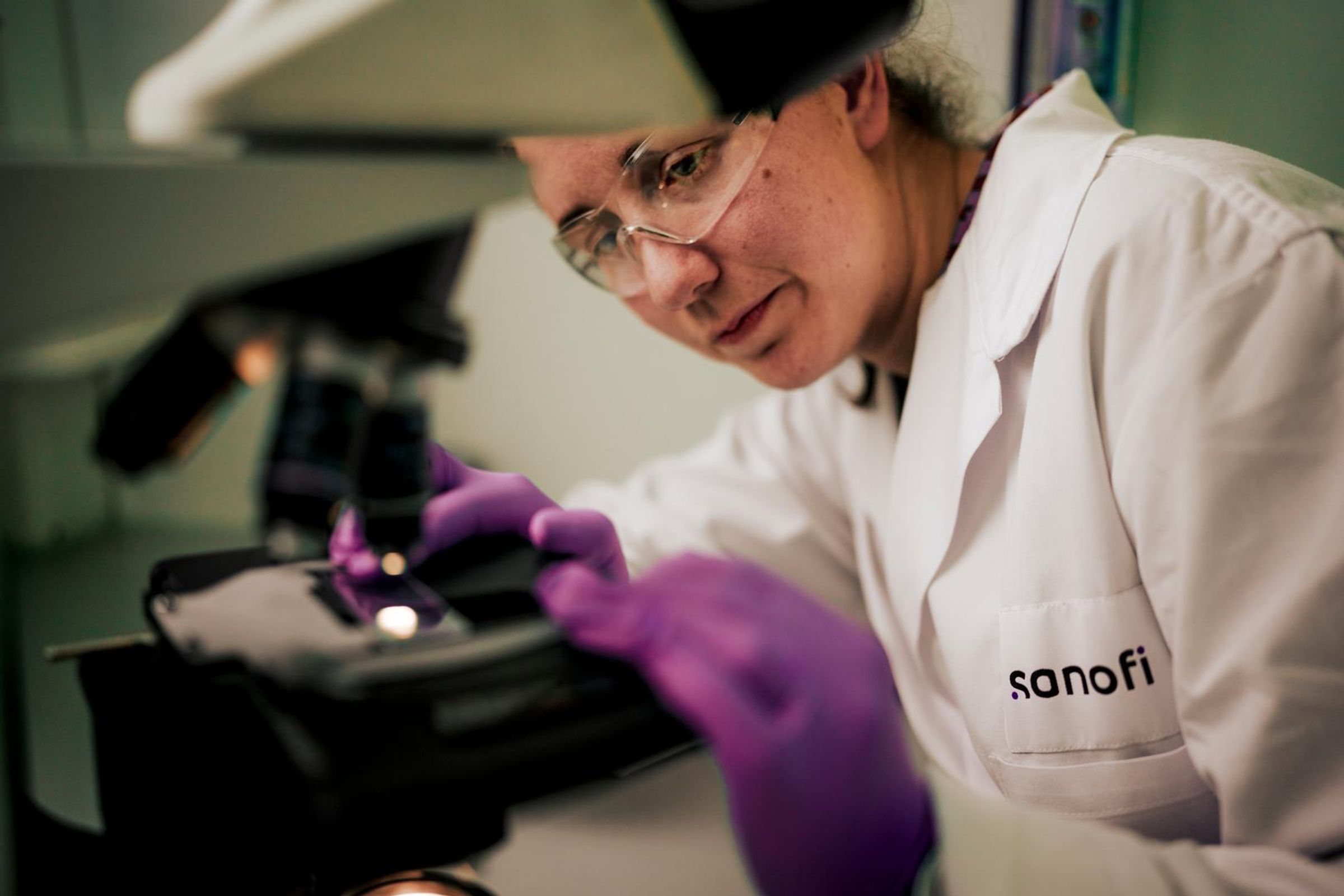 An-Sophie Claerbout is wearing a white lab coat and purple gloves, and prepares a slide in a microscope